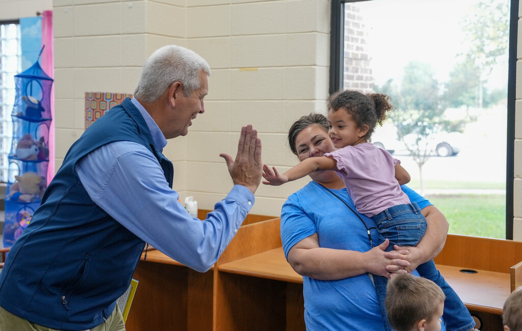 A man with gray hair and a blue vest high-fives a child in a blue shirt.