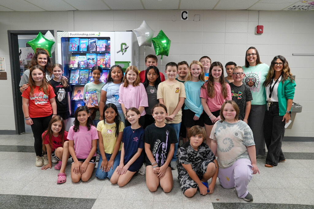 Group of children and adults posing for a photo in front of a snack vending machine.