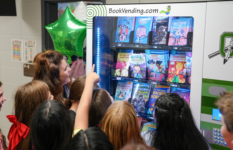 Crowd of students point to a book vending machine