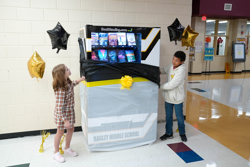 A male and female student unwrap a book vending machine