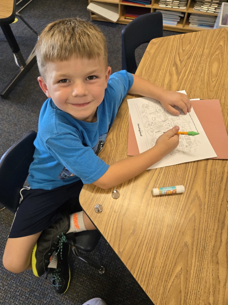 a boy smiling while he writes on a paper at his desk