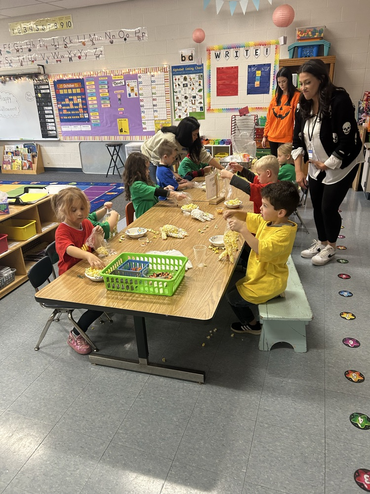 two adults standing over students in class