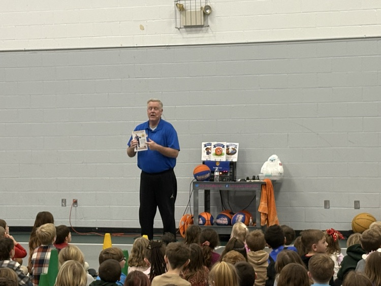 man holding a book in front of children sitting on the floor