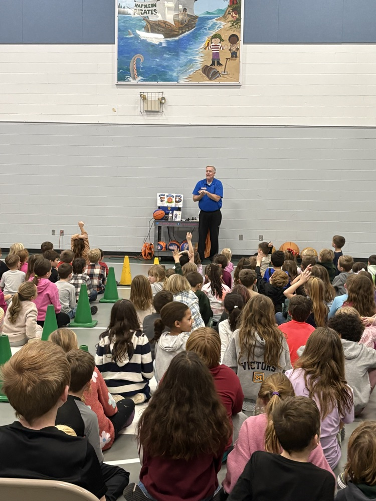 children sitting on the floor watching man perform basketball tricks