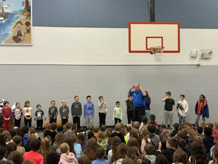 students standing at the front with man performing and students sitting on the floor watching