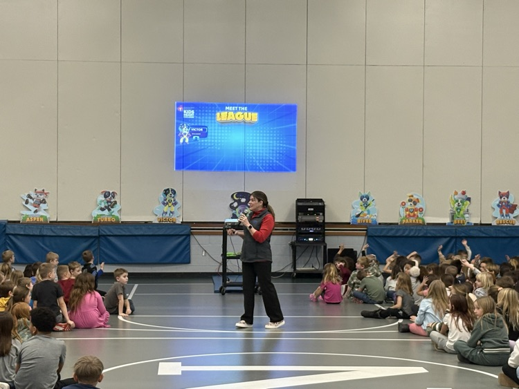 woman speaking in front of the students with a screen behind her