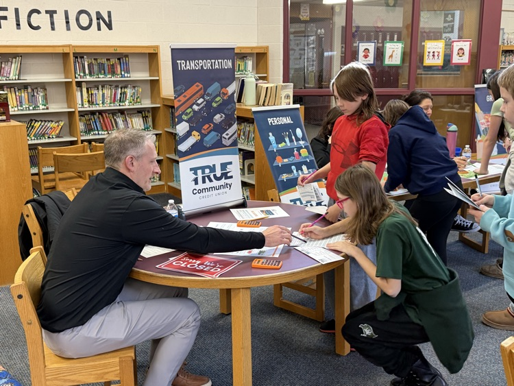 man helping students at table at True Community Reality Fair