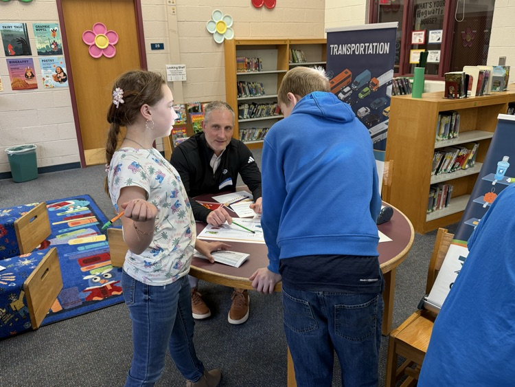 students at table with adult participating in True Community Reality Fair