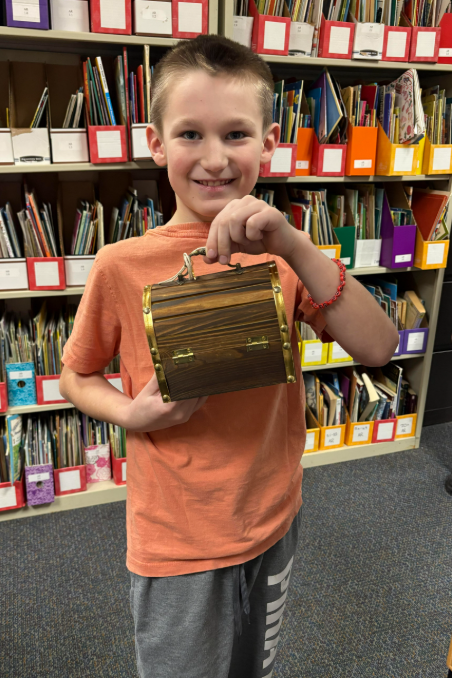 boy student holding a treasure chest in a room full of books 
