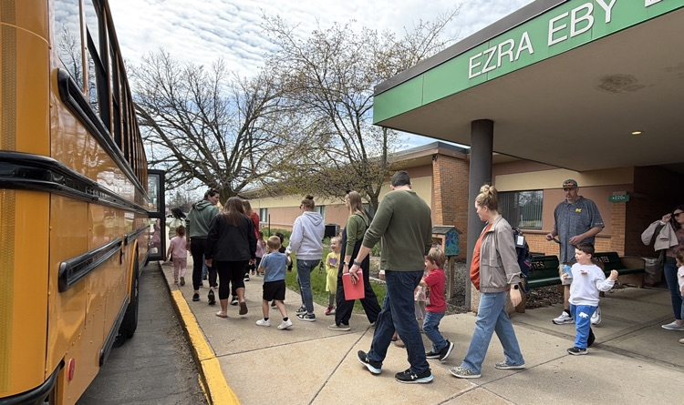 students with their parents boarding a bus in front of a school 