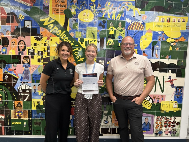 two women and a man standing in a school holding a check