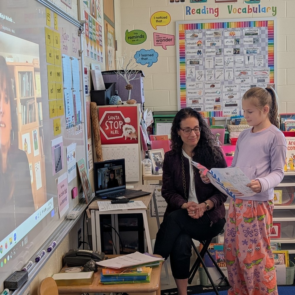 Student stands next to teacher whole looking at a paper.