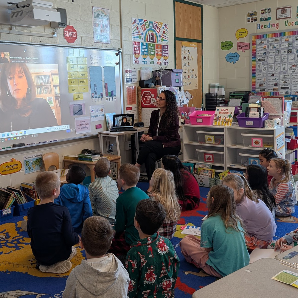 Elementary students sit on the rug and look up at a projected screen showing author Jill Lauren.