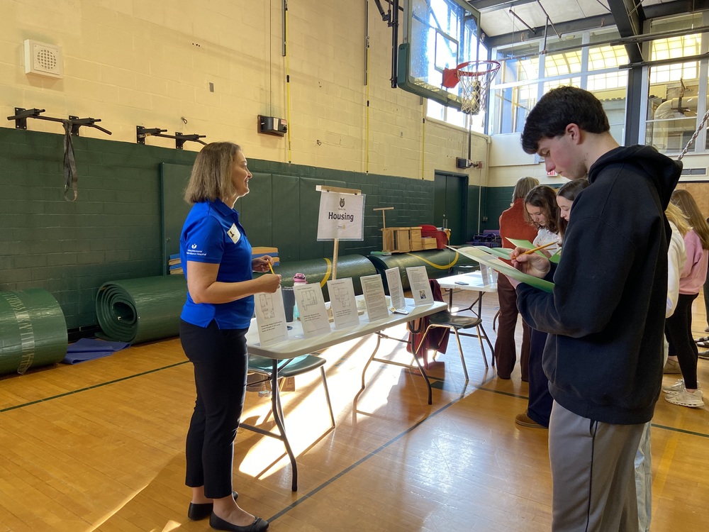 A community members guides students works with students at the reality fair's housing table.