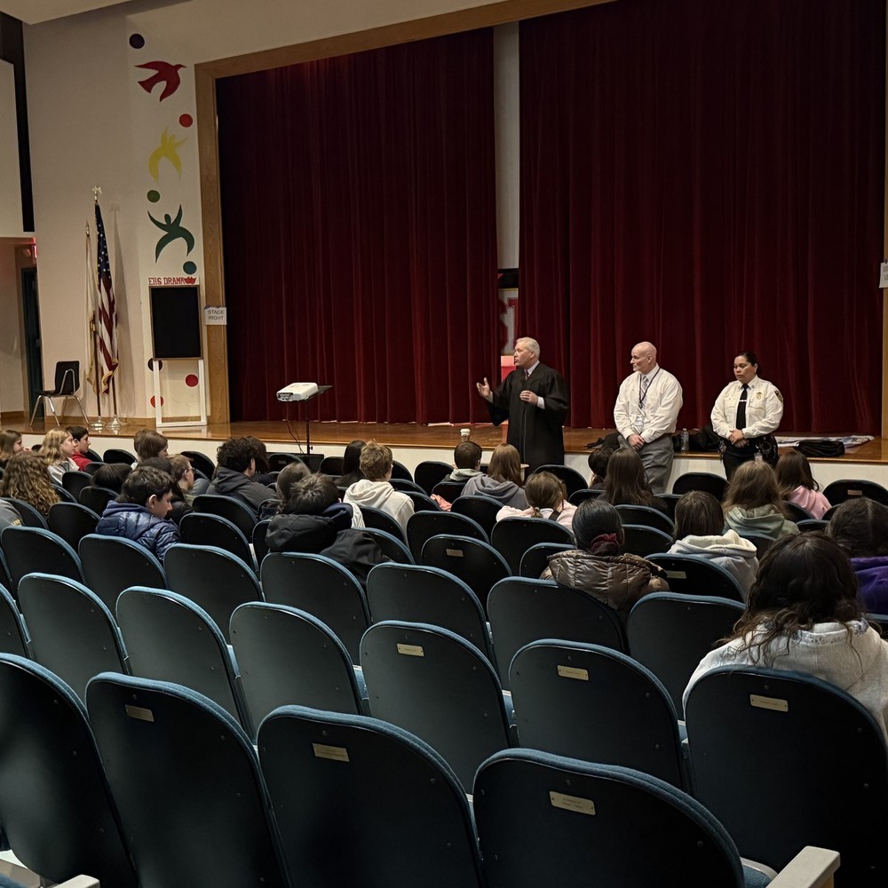 Students sit in auditorium seats while a judge presents