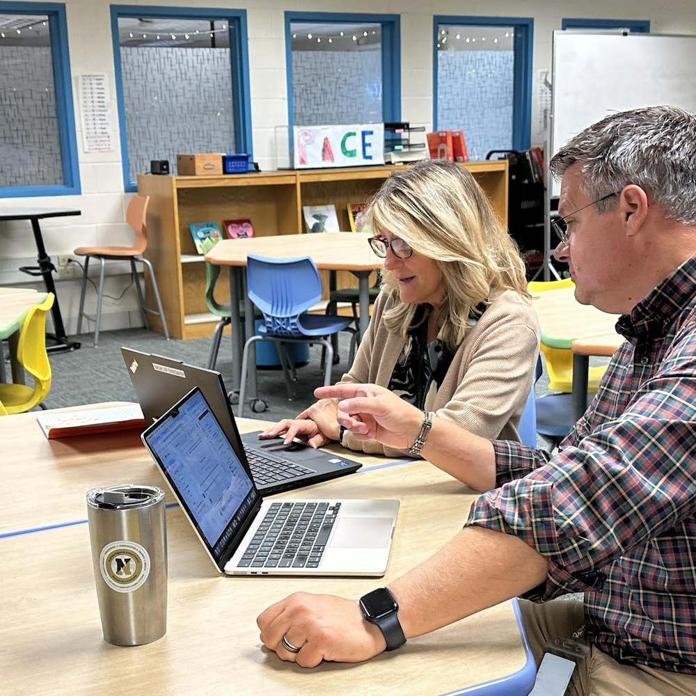 Two NRSD staff members sit together looking at laptops.