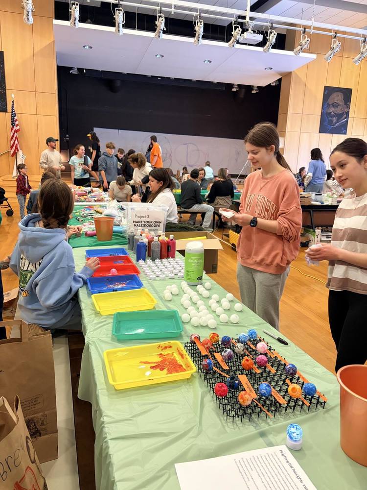High school students help elementary students at a craft table.