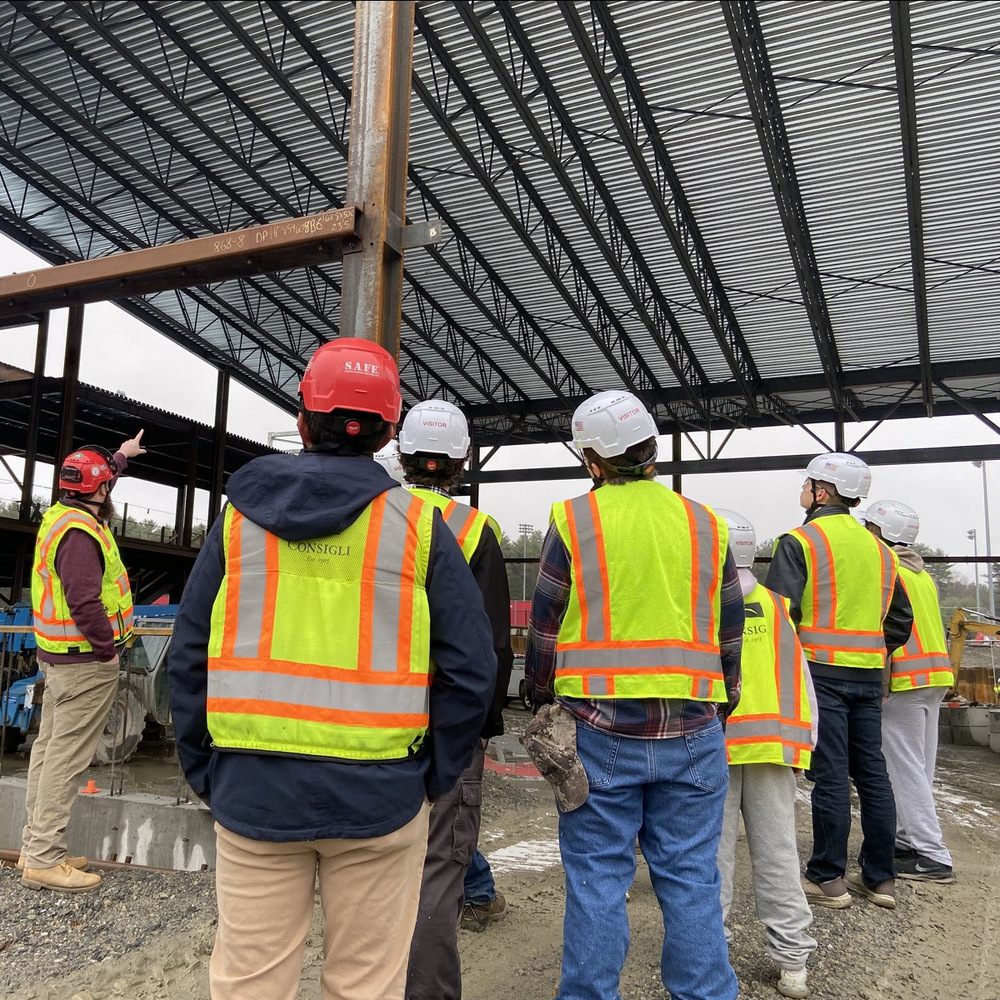 NRHS students stand inside of the new high school build wearing hard hats and high viz vests.