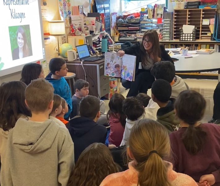 Representative Kilcoyne holds a book up to a group of fourth grade students.