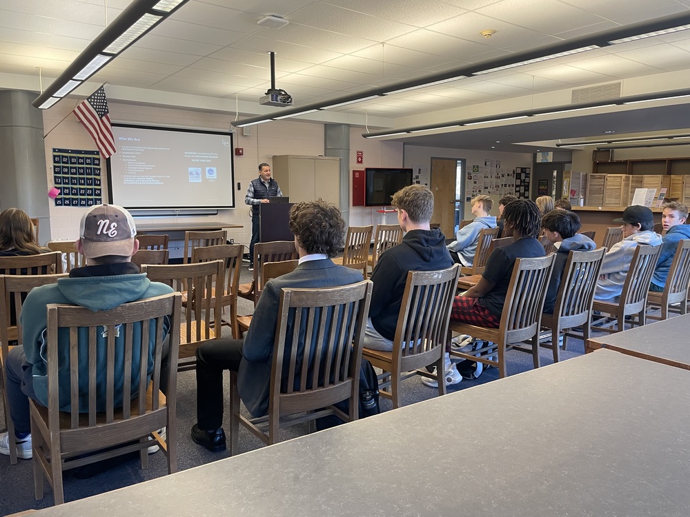 A guest speaker presents to students seated in the library.