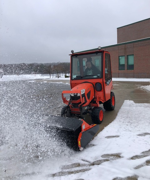 A custodian at MRE drives an orange snow blower through the parking lot.