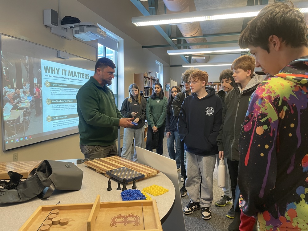 A teacher shows a group of 8th grade students high school projects.