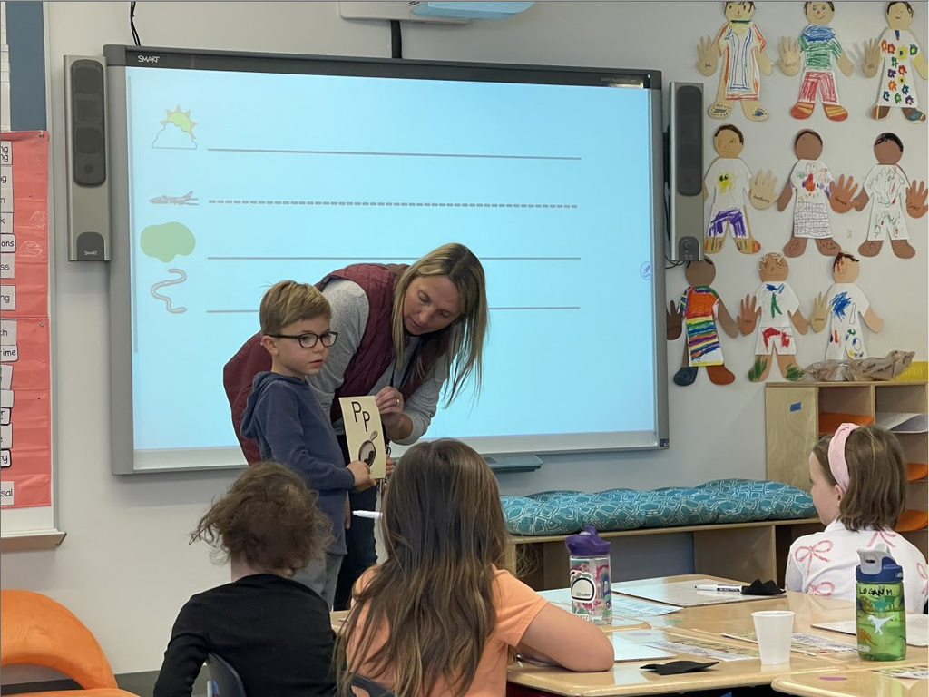 teacher and student hold up the letter P in front of the class