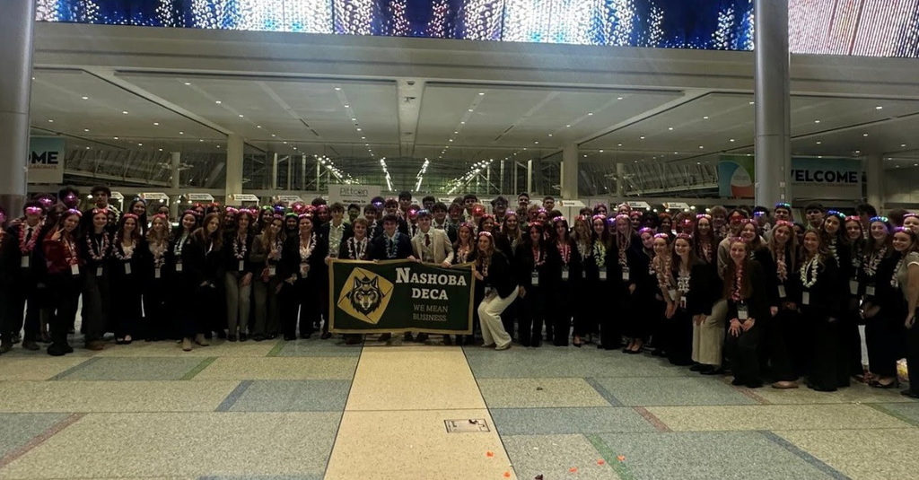 a large group of students stands together holding a Nashoba DECA banner
