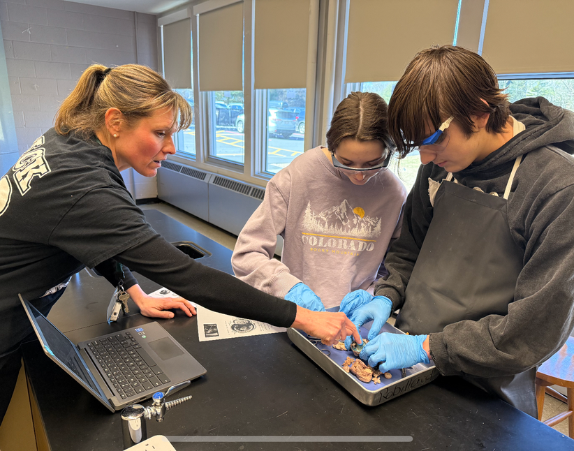 two students work on a dissection while they're teacher points at it