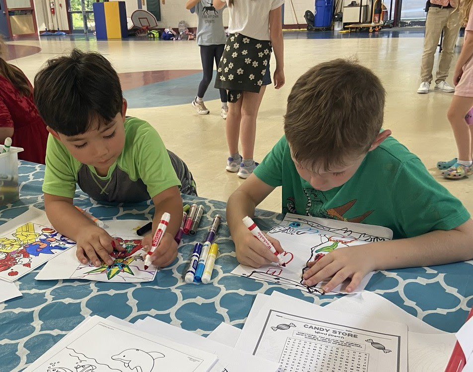 Two students sit at a table in the Emerson building cafeteria coloring with markers.