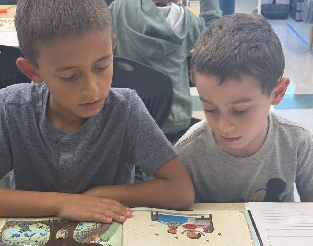 Two students sit next to each other reading a picture book.
