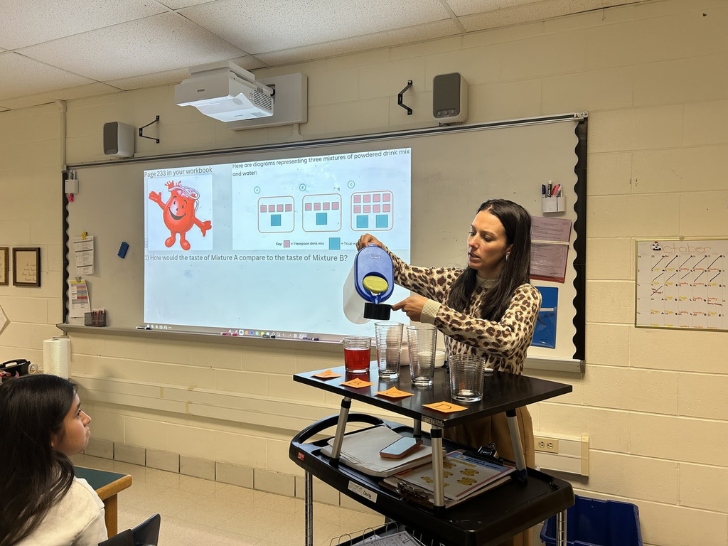 A middle school teacher pours water and Kool-Aid into a measuring cup as part of a lesson on ratios.