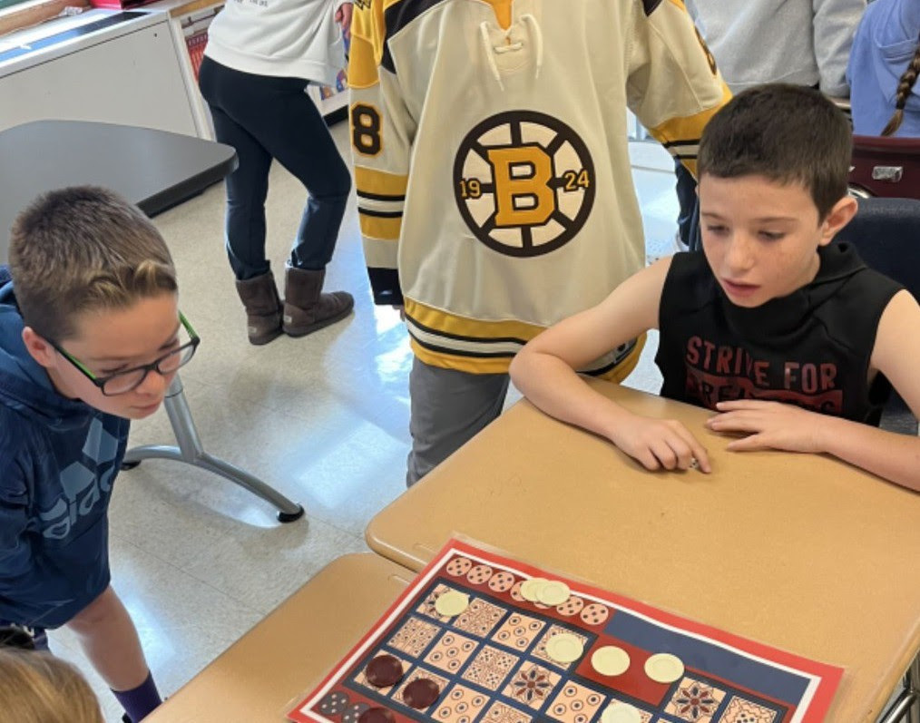 A small group of students stands around a board game that is colored red, white, and blue.