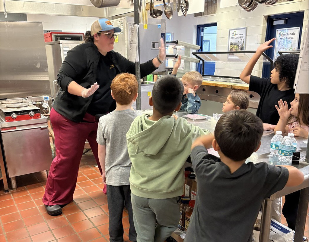 A staff member high fives elementary school students in the cafeteria.