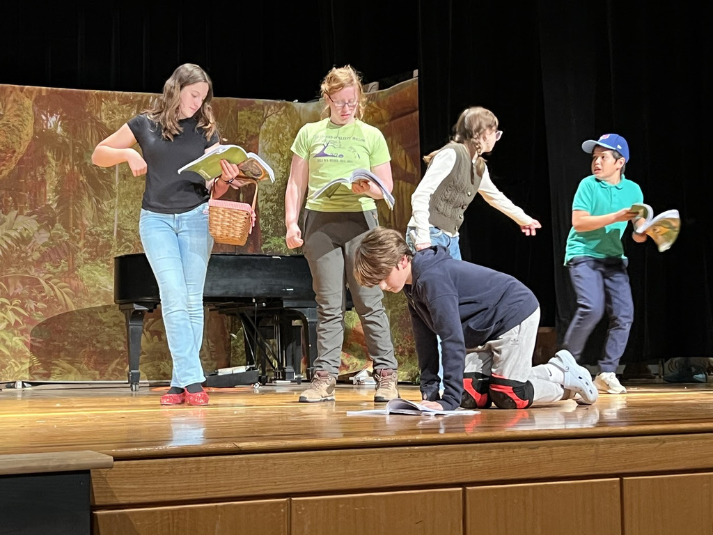 Hale middle school students stand holding scripts and props on stage.