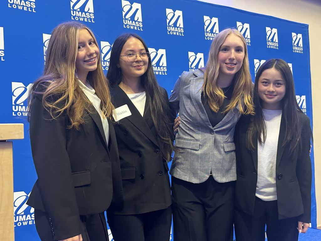 Four NRHS DECA students pose in business attire at UMass Lowell during the Difference Maker Competition.
