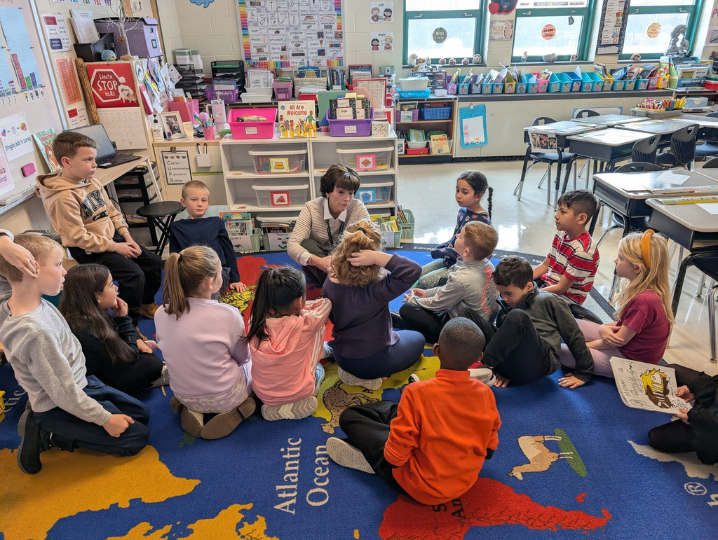 Assistant Superintendent Friend sits with MRE students on the rug chatting.