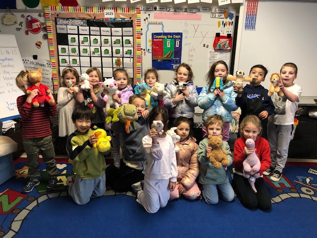 MRE Kindergarten students pose together on a rug in their pajamas with stuffed animals during spirit week.