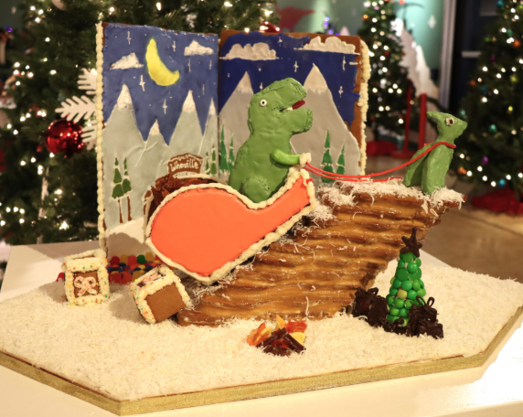 A gingerbread house with a dinosaur riding a sleigh.