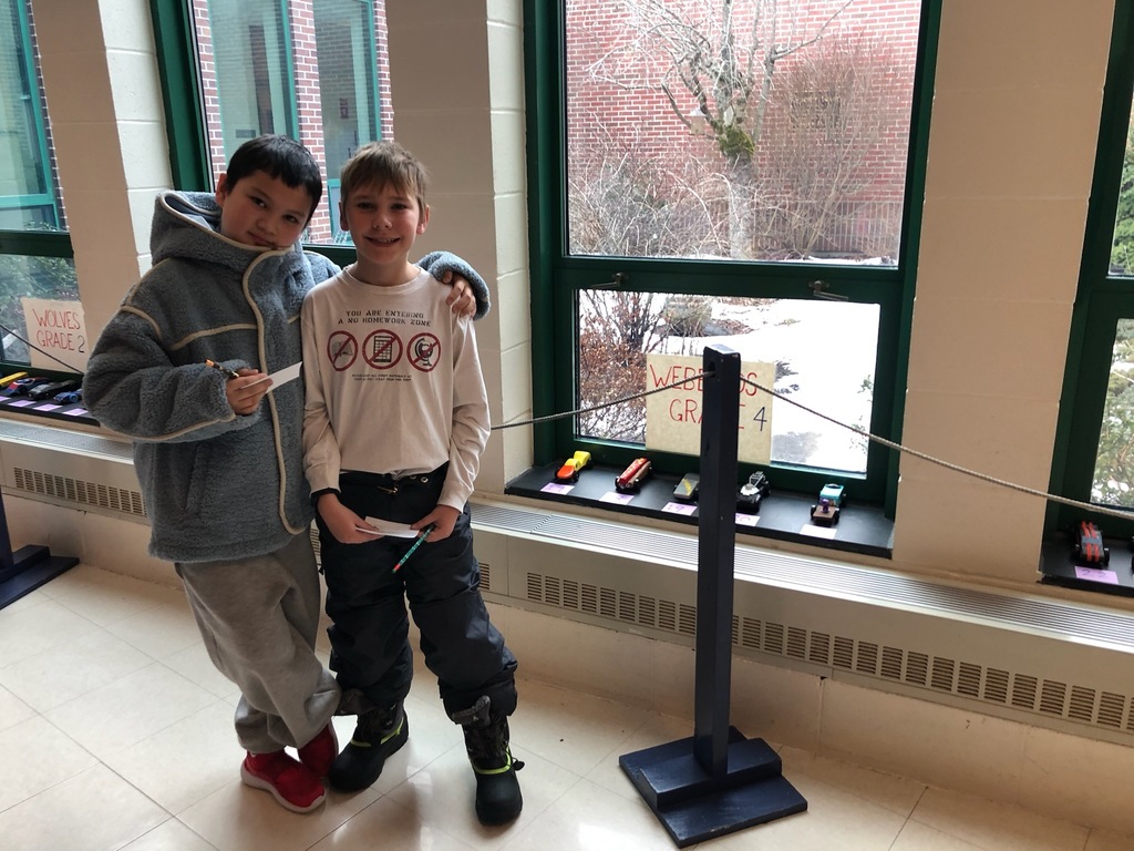 Two students stand in front of miniature model cars.