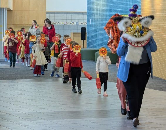 Principal Coppinger leads kindergarten students down the hall with dragon masks for the Lunar New Year.