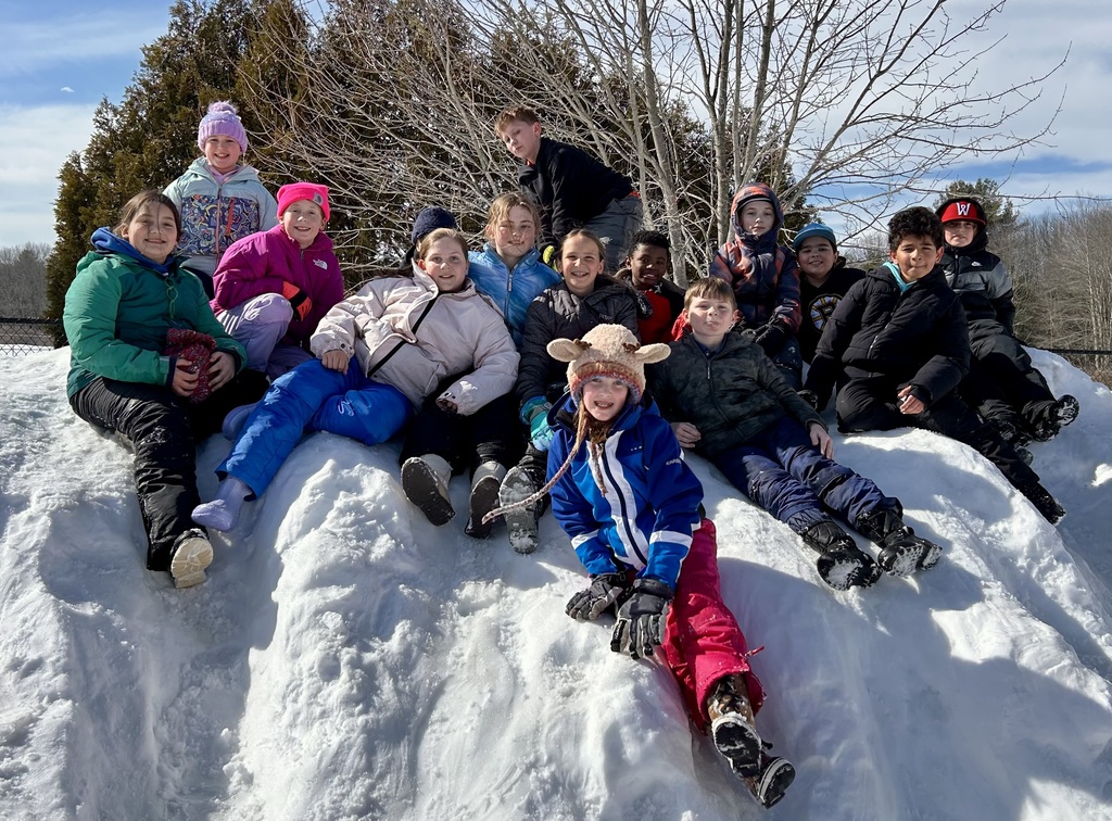MRE students sit and pose for a photo on a snowbank on the playground.