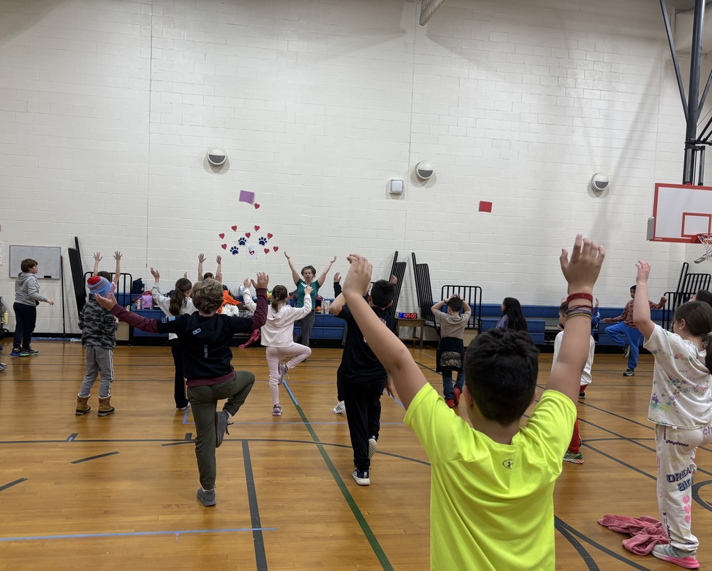 In the MRE gym students stand on one leg with their hands in the air.