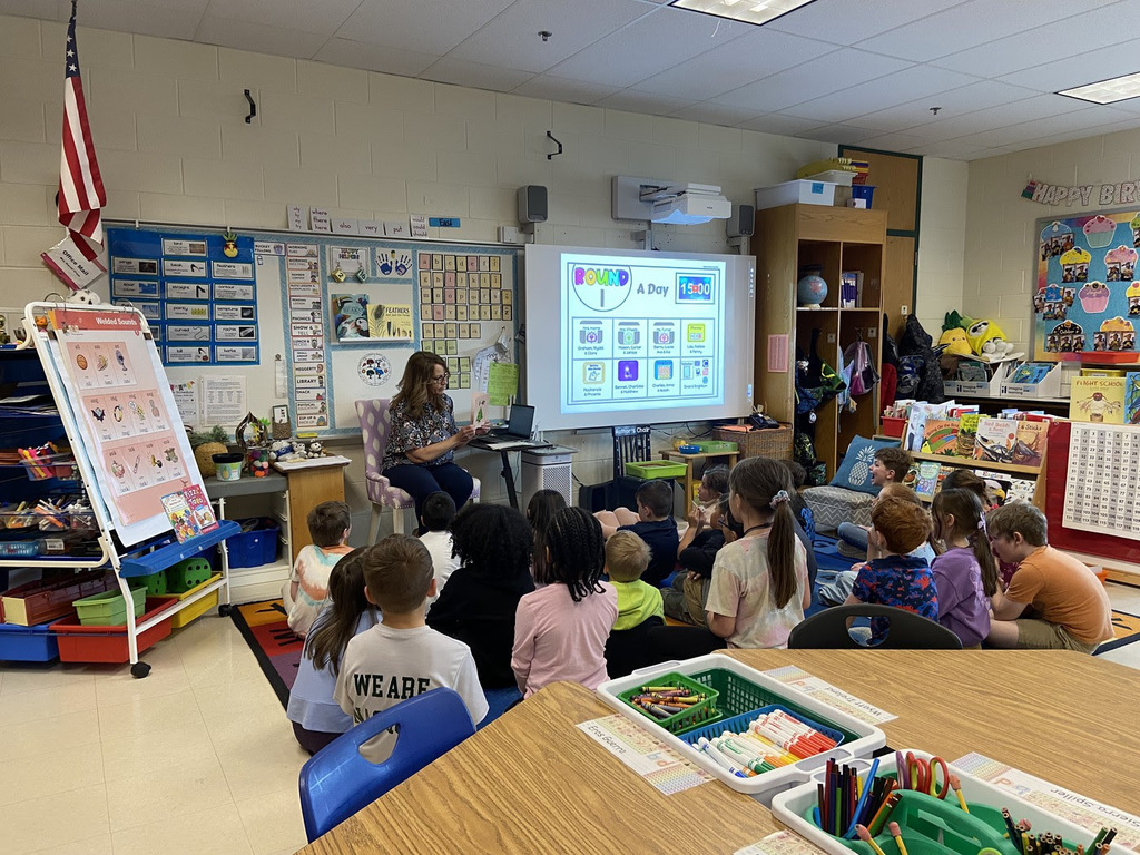 MRE students sit on the rug and watch their teacher.