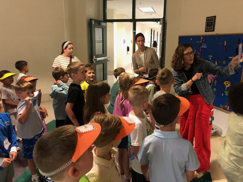 Kindergarten students stand in an MRE hallway listening to a teacher.