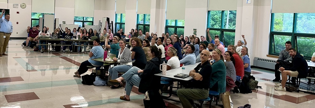 Middle school educators from around the district gather in the FSS auditorium, waving at the camera.
