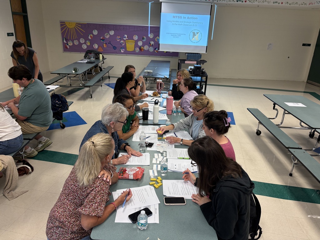 NRSD educators sit together at a cafeteria table in MRE looking at a presentation.