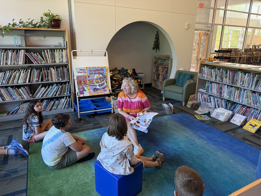 Students sit in the library listening to their teacher read a book.