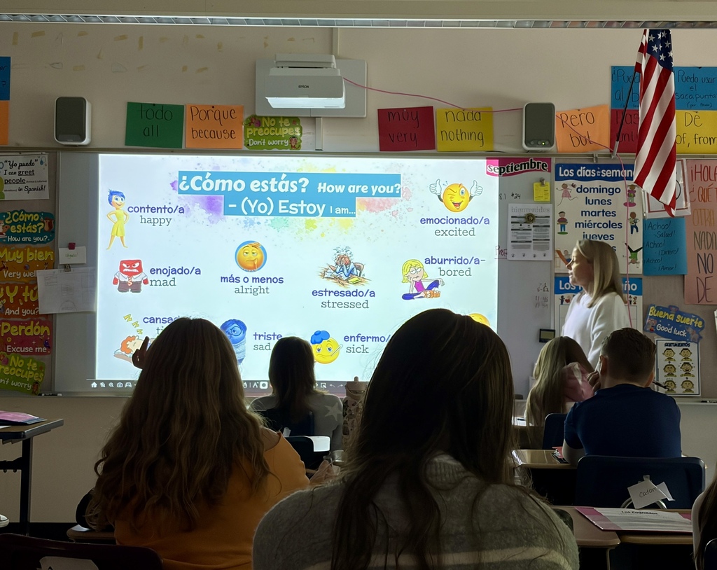 FSS students sit in Spanish class looking at a projection that features the questions "Como estas?"
