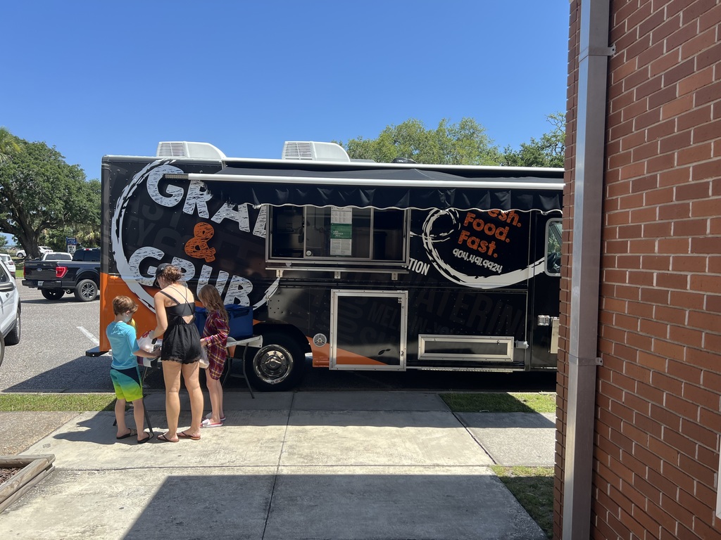 Children and an adult receiving meals from the “Grab & Grub” food truck parked outside a school building.
